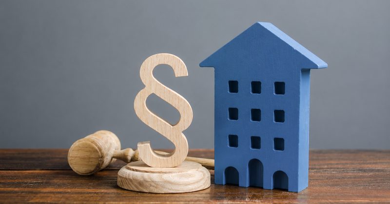 Blaues Modellhaus neben einem hölzernen Paragraphenzeichen und einem Richterhammer, Symbolbild zur WEG-Reform 2020